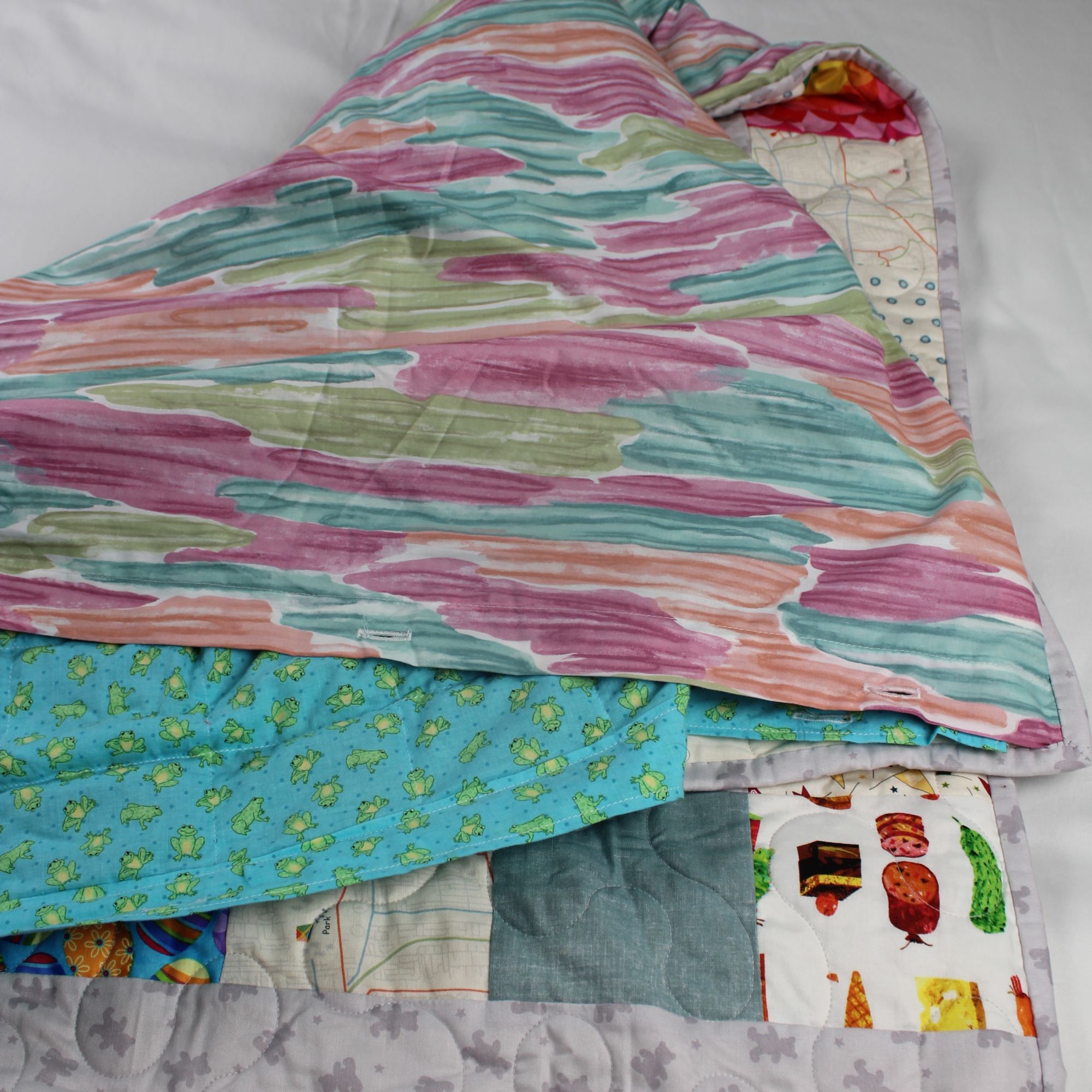 Hopscotch Storytime quilt with pastel watercolor backing folded back to reveal the turquoise frog print insert underneath