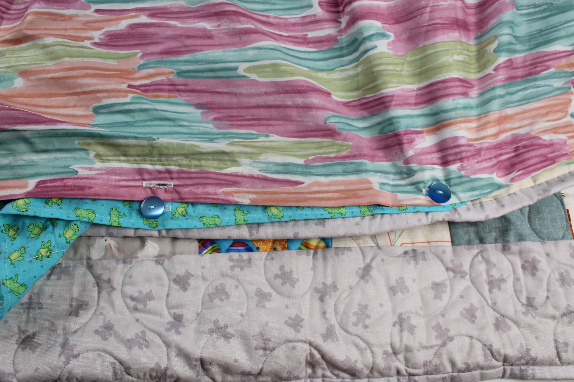 Button-closure opening on the pastel watercolor backing of the Hopscotch Storytime quilt, revealing the turquoise frog print insert